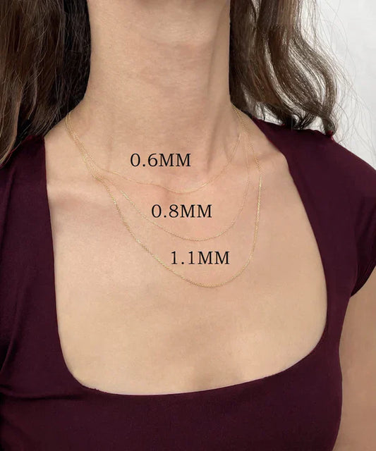 Close-up of a woman wearing three layered gold chain necklaces in different thicknesses labeled 0.6mm, 0.8mm, and 1.1mm
